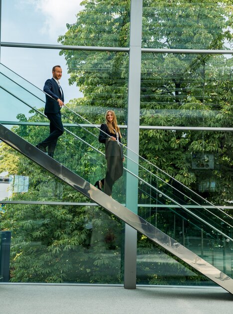 Two professionals in business attire descending a glass staircase. | © Graz Tourismus - Mias Photoart