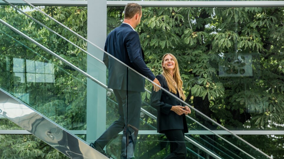 Two people in formal attire ascending stairs at Messe Graz, surrounded by modern architecture and greenery. | © Graz Tourismus - Mias Photoart
