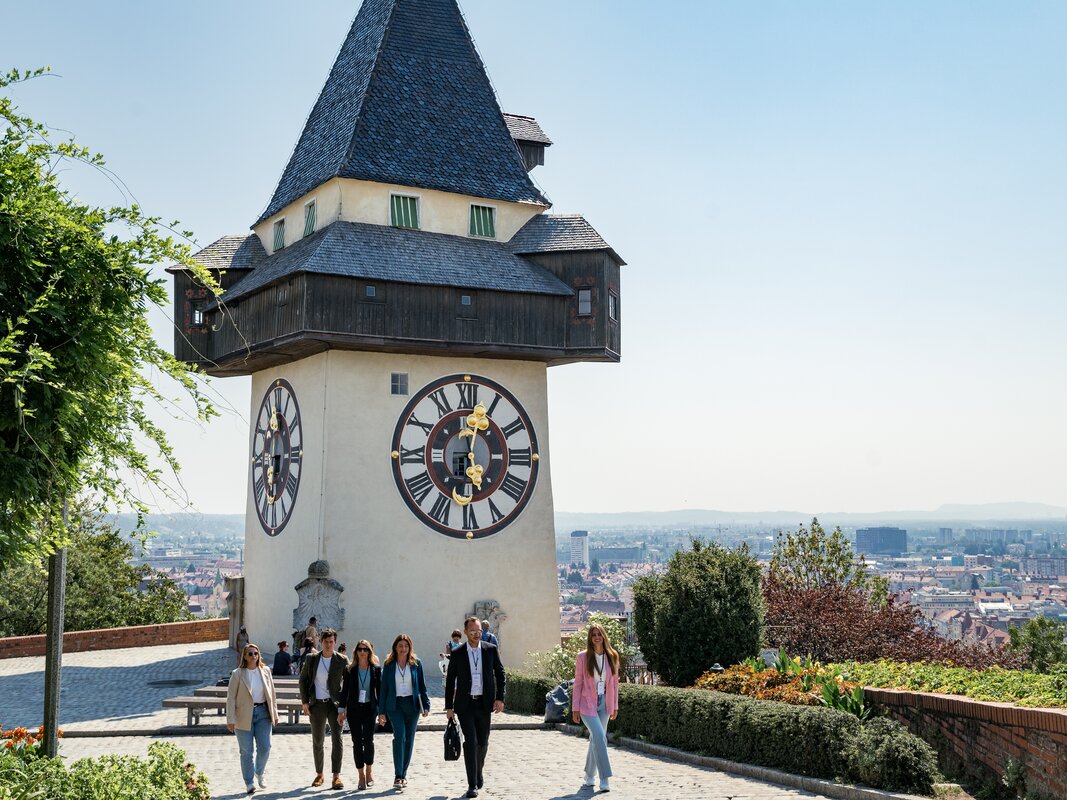 Die Grazer Uhrturm zeigt eine Gruppe von Menschen bei einem Spaziergang über Graz. | © Graz Tourismus - Mias Photoart