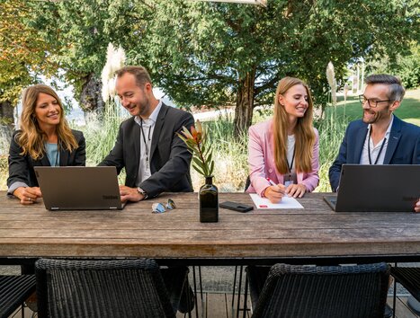 Four people working on laptops during an outdoor business meeting. | © Graz Tourismus - Mias Photoart