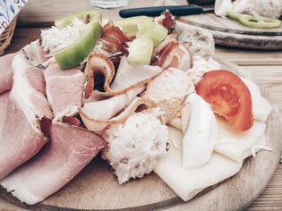 A selection of cold meats, cheese, and fresh vegetables on a wooden board. | © Nomad Epicureans