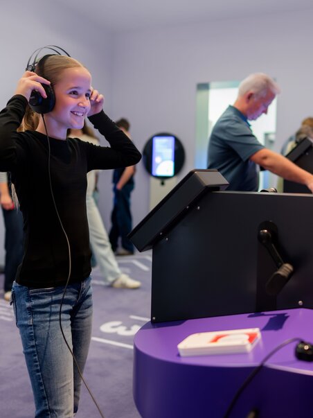 A smiling teenager wearing headphones explores interactive displays at the museum. | © Stellework