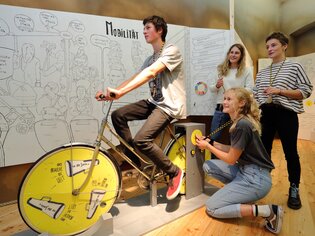 Jugendliche erleben Mobilität auf einem Rad im Museum. | © Universalmuseum Joanneum / J. Kucek