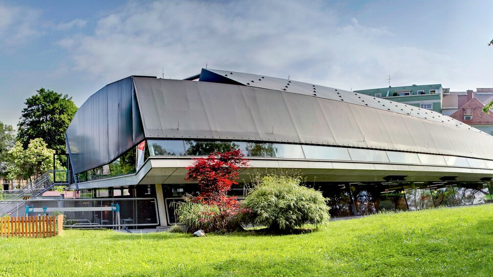 Das Bild zeigt einen modernen Bau in Graz, umgeben von grüner Wiese und Bäumen. | © Hannes Loske