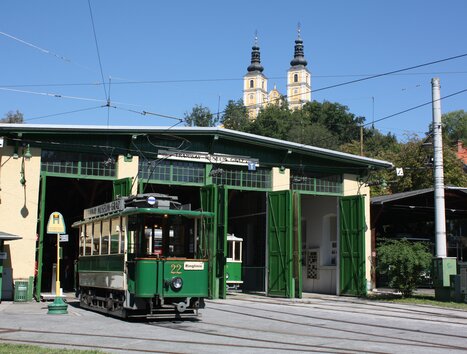 Una tramvia storica davanti a un'officina a Graz, con torri sullo sfondo. | © Tramway Museum Graz