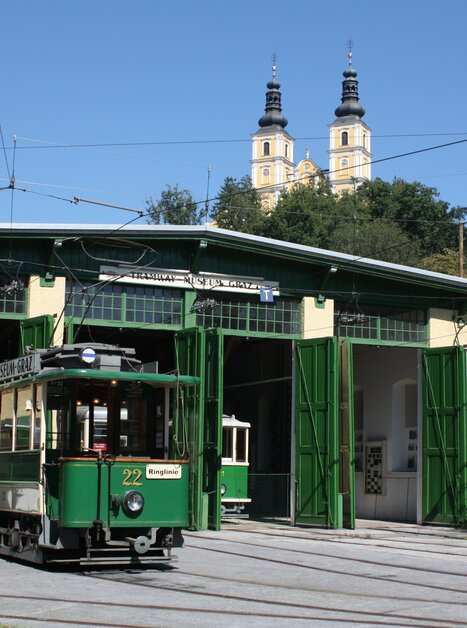 Una tramvia storica davanti a un'officina a Graz, con torri sullo sfondo. | © Tramway Museum Graz
