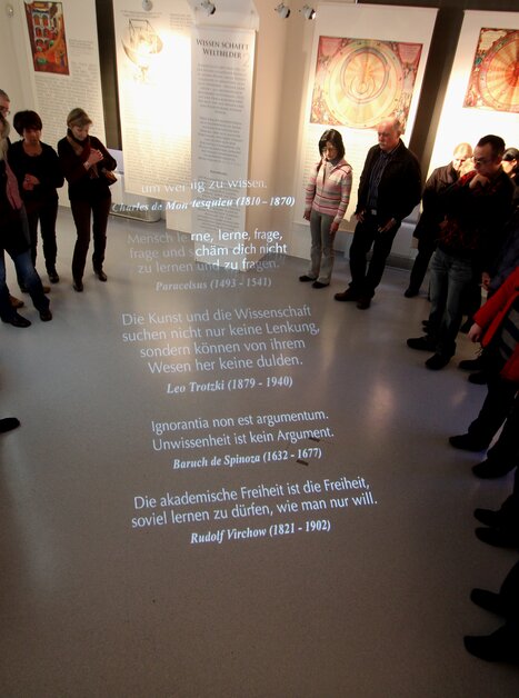 Visitatori al museo che ascoltano citazioni su scienza e libertà proiettate sul pavimento. | © UniGraz@Museum