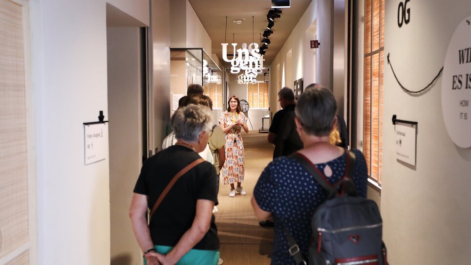 Führerin mit Besuchern im Volkskundemuseum, Text im Bild lesbar. | © J.J. Kucek