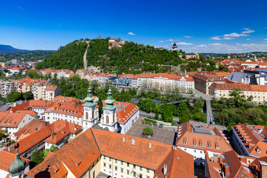 Blick auf Graz mit Schlossberg, Mur und Murinsel und Dachlandschaft im Vordergrund. | © Graz Tourismus - Harry Schiffer