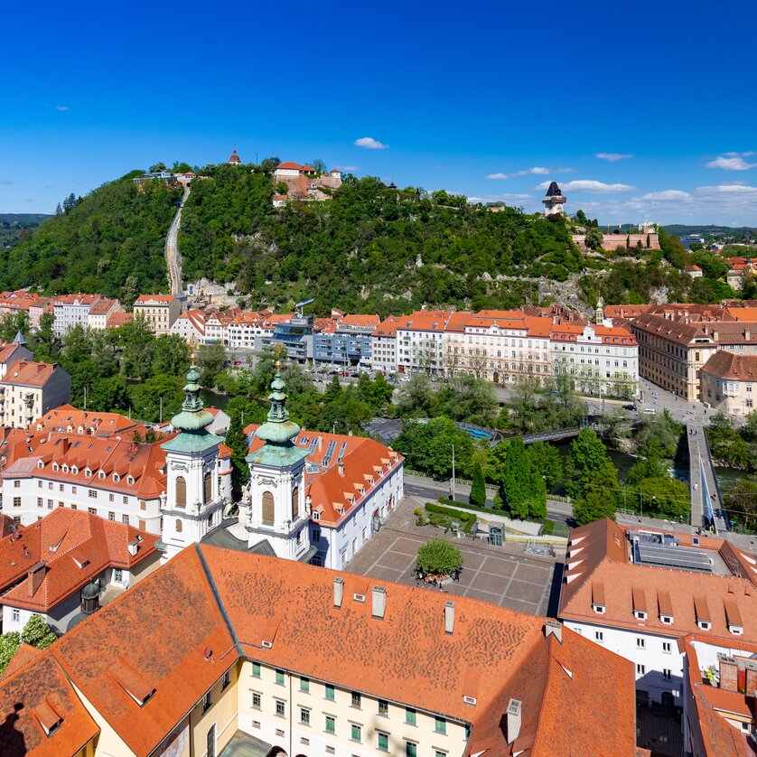 Blick auf Graz mit Schlossberg, Mur und Murinsel und Dachlandschaft im Vordergrund. | © Graz Tourismus - Harry Schiffer