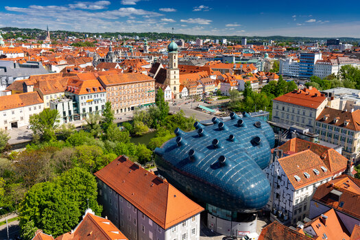 Blick auf Graz mit dem blauen Kunsthaus zwischen historischen Dächern. | © Graz Tourismus - Harry Schiffer