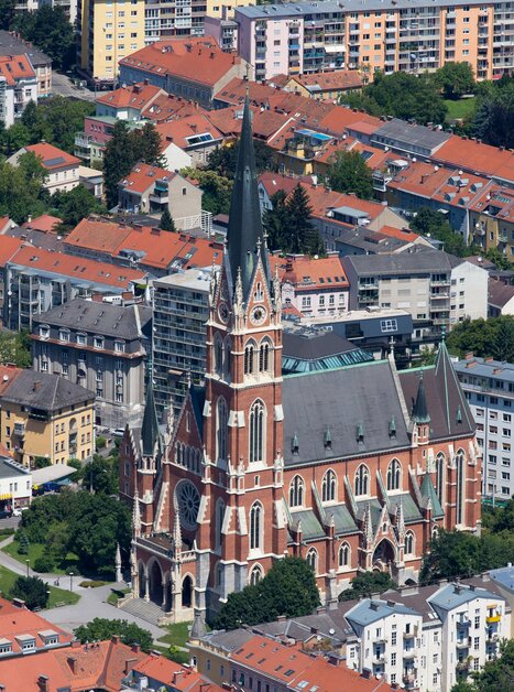 Vista sulla città di Graz con una chiesa prominente circondata da edifici residenziali. | © Graz Tourismus - Harry Schiffer