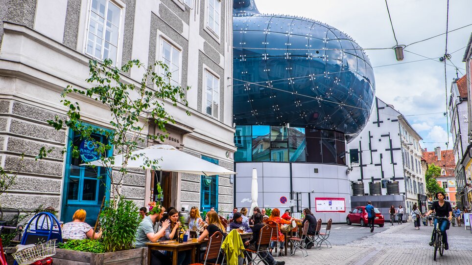 View of Kunsthaus Graz and a street café with guests. | © Becki Enright_Boarders of Adventure