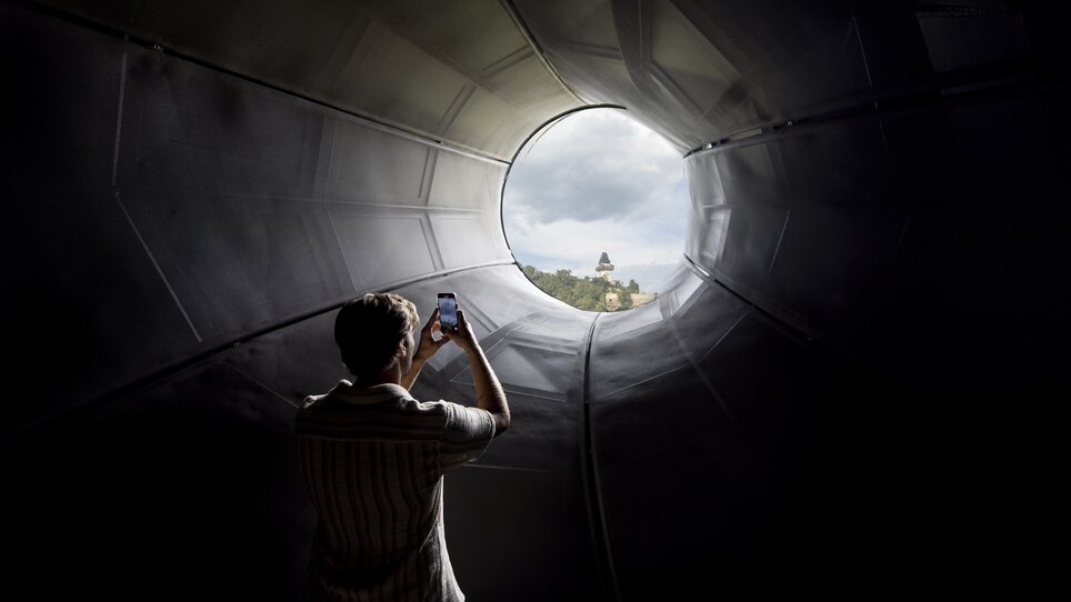 Visitor photographs Graz Clock Tower through Kunsthaus Graz. | © Graz Tourismus - Tom Lamm