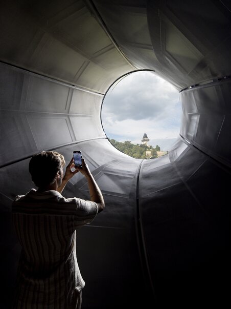Visitatore fotografa la Torre dell'Orologio di Graz attraverso il Kunsthaus Graz. | © Graz Tourismus - Tom Lamm