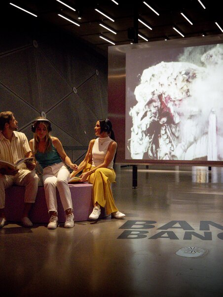 Tre persone nel Kunsthaus Graz, davanti a un video con il testo BANG. BANG. | © Graz Tourismus - Tom Lamm