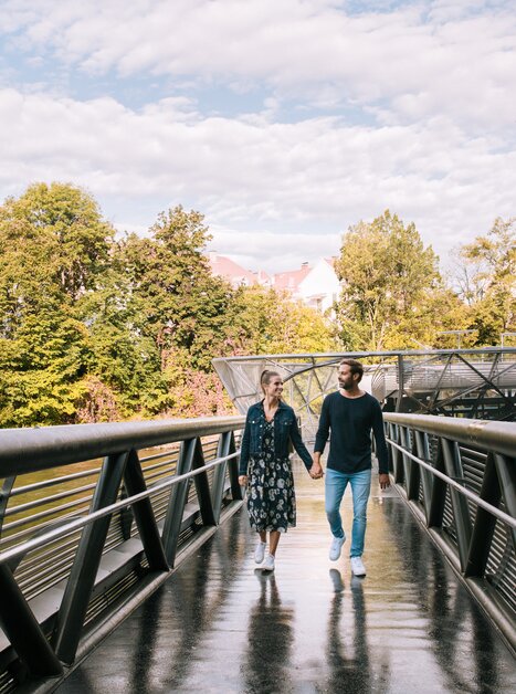 Couple walking on the Mur Island in Graz, surrounded by trees. | © Graz Tourismus