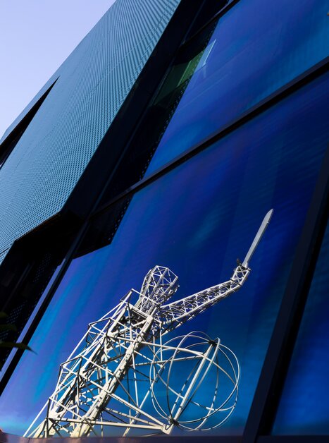 Reflexion der eleganten Lichtschwert Statue neben der Grazer Oper in einem blauen Fenster. | © Graz Tourismus - Harry Schiffer
