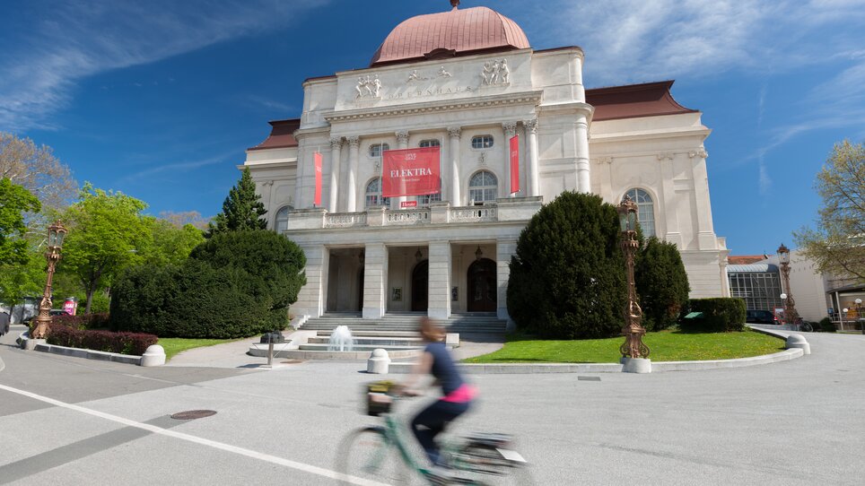 Die Oper Graz mit lebendigem Umfeld und einem Radfahrer auf der Straße. | © Graz Tourismus - Harry Schiffer