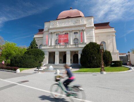 L'Opera Graz con un ambiente vivace e un ciclista sul marciapiede. | © Graz Tourismus - Harry Schiffer
