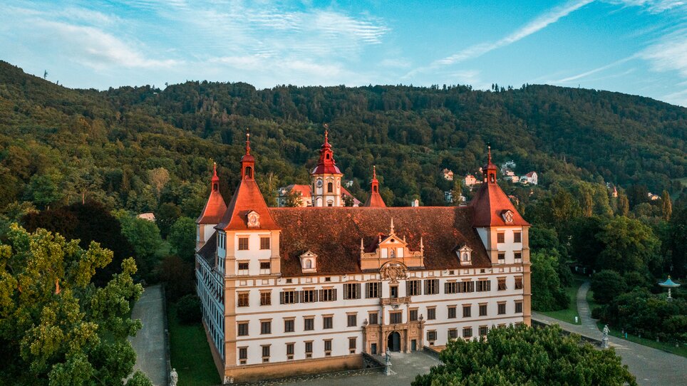 A view of Eggenberg Palace, surrounded by trees and mountains. | © Graz Tourismus - Mias Photoart