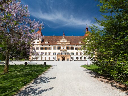 Castello di Eggenberg a Graz, circondato da alberi in fiore e cielo sereno. | © Graz Tourismus - Harry Schiffer