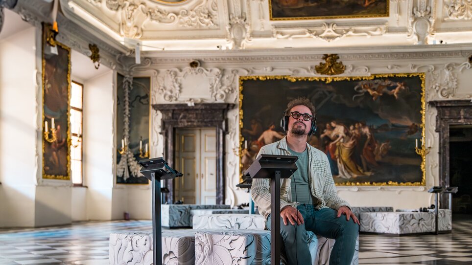 Mann mit Kopfhörern sitzt in einem kunstvollen Raum. | © Graz Tourismus - Mias Photoart