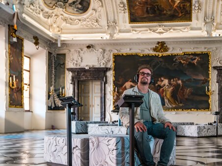 Mann mit Kopfhörern sitzt in einem kunstvollen Raum. | © Graz Tourismus - Mias Photoart