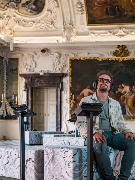 Man wearing headphones sitting in an ornate room. | © Graz Tourismus - Mias Photoart