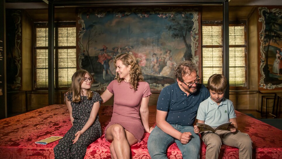 Eine Familie sitzt zusammen, zwei Kinder und zwei Erwachsene in einem historischen Ambiente im Schloss Eggenberg. | © Graz Tourismus - Mias Photoart