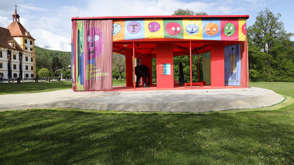 Bunter Pavillon mit grafischen Elementen in einem Park, mit einem Besucher. | © Universalmuseum Joanneum - J. Kucek © Bildrecht Wien 2025