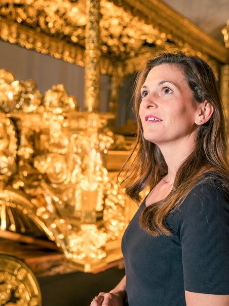 Eine Frau mit brünettem Haar steht vor einem prunkvollen goldenen Kunstwerk. | © Graz Tourismus - Mias Photoart