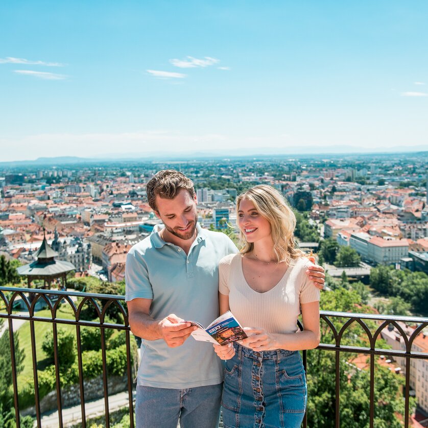 Ausblick vom Grazer Schlossberg | © Graz Tourismus - Mias Photoart Paar genießt den Ausblick über Graz vom Schlossberg. Die beiden betrachten einen Prospekt von Graz. | © Graz Tourismus - Mias Photoart