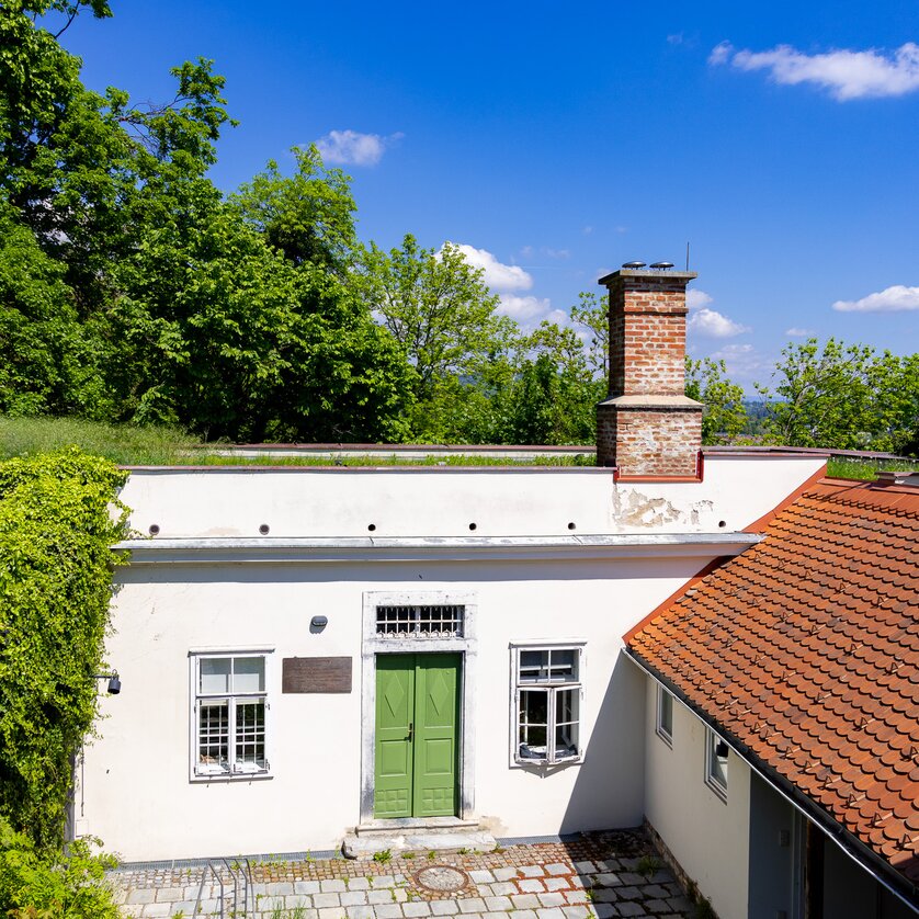 Cerrini-Schlössl am Schlossberg in Graz | © Graz Tourismus - Harry Schiffer Das Cerrini-Schlössl mit grünem Eingang und Kamin, umgeben von Bäumen und blauem Himmel. | © Graz Tourismus - Harry Schiffer