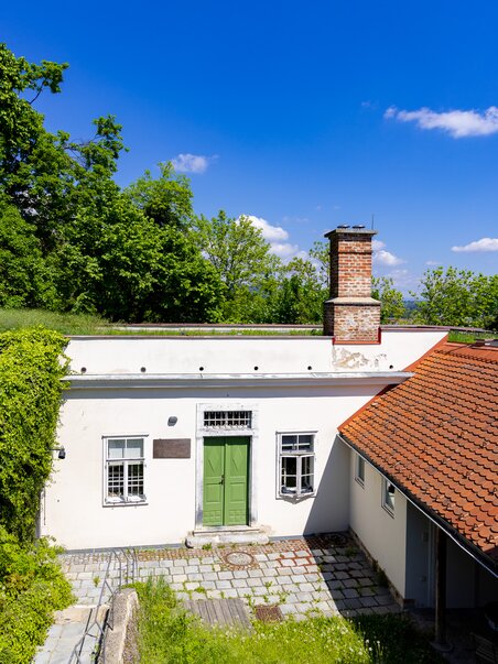 Das Cerrini-Schlössl mit grünem Eingang und Kamin, umgeben von Bäumen und blauem Himmel. | © Graz Tourismus - Harry Schiffer