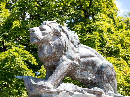 Bronze lion sculpture on Schlossberg in Graz with green trees. | © Graz Tourismus - Harry Schiffer