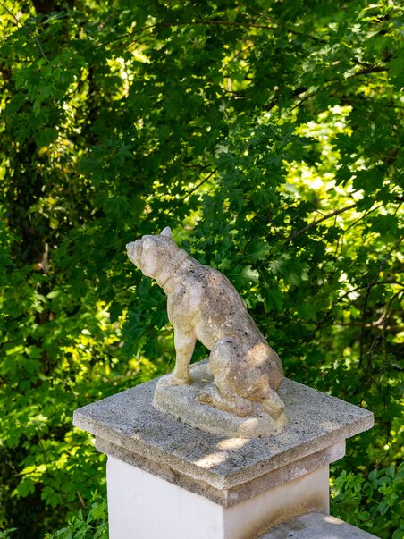 A stone dog sculpture in front of a green tree backdrop. | © Graz Tourismus - Harry Schiffer