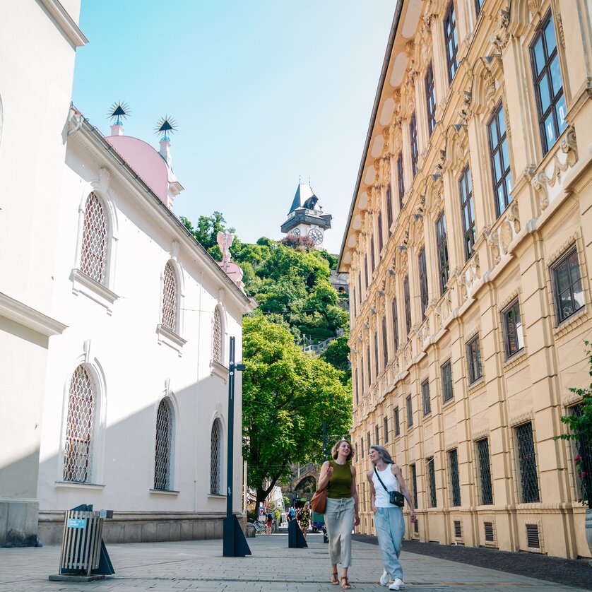 Zwei Frauen spazieren am Schlossbergplatz in Graz, Uhrturm im Hintergrund. | © Graz Tourismus - Mias Photoart