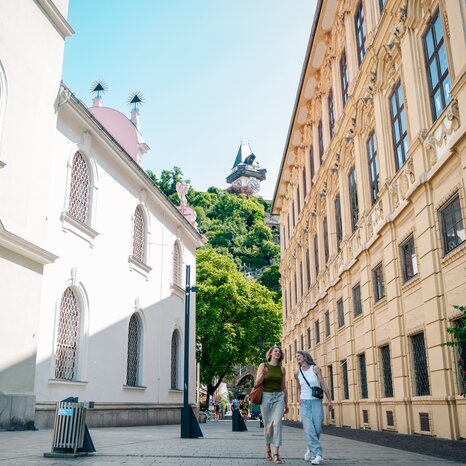 Two women walking at Schlossbergplatz in Graz, Clock Tower in the background. | © Graz Tourismus - Mias Photoart