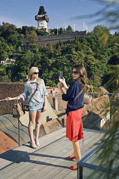 Zwei Frauen posieren im Café Freiblick mit dem Uhrturm am Grazer Schlossberg im Hintergrund. | © Graz Tourismus - Toni Muhr