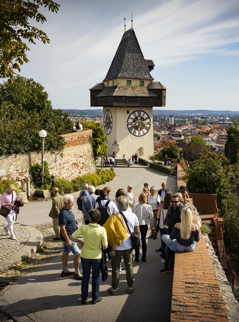 Visitors exploring the Schlossberg with a view of the Graz Clock Tower and the city. | © Graz Tourismus - Werner Krug