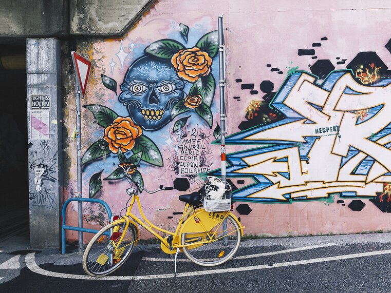 Yellow bicycle in front of a wall featuring colorful graffiti of a skull and roses. | © Adeline Gressin