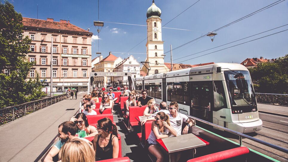 Passengers on the open-top bus drive through Graz, with the Franciscan Church in the background. | © Lupi Spuma