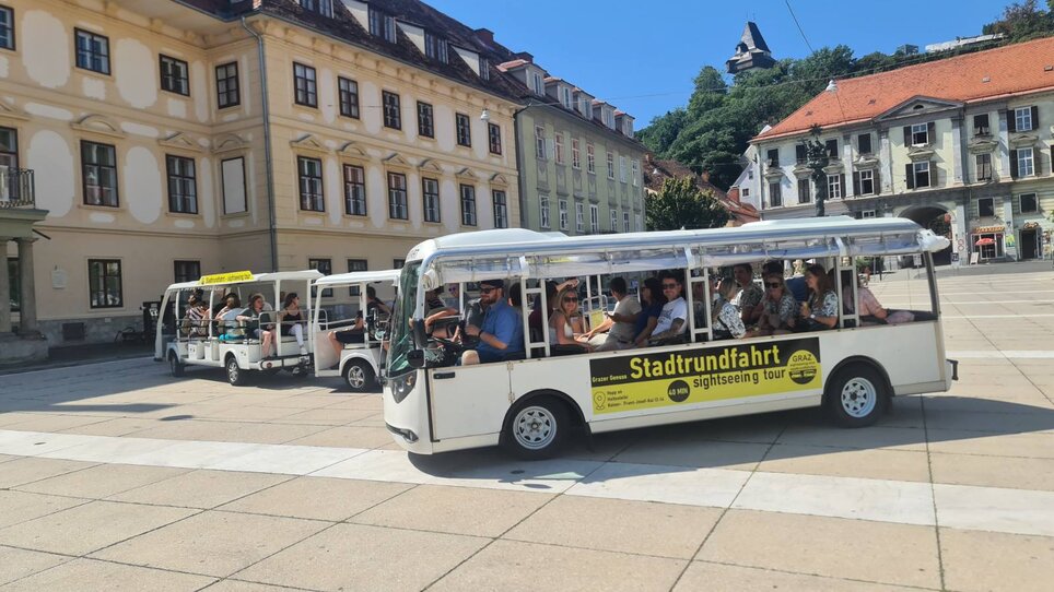 Elektroshuttle auf Stadtrundfahrt in Graz. Grazer Uhrturm und historische Gebäude im Hintergrund. | © Graz Stadtrundfahrten