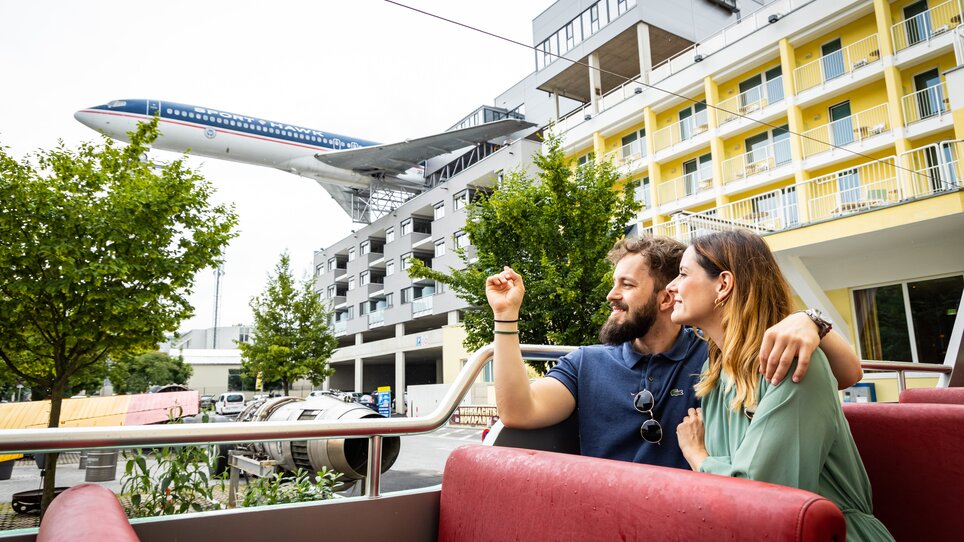 Paar genießt die Aussicht bei einer kulinarischen Tour mit dem Cabriobus - im Hintergrund ein Flugzeug des Flugzeug-Restaurants NOVAPARK. | © Graz Tourismus - Werner Krug