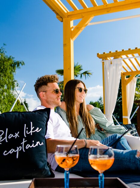 Coppia che si rilassa in un lounge con cocktail e un messaggio sul cuscino. | © Region Graz - Mias Photoart