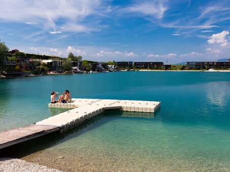 Three people sit on a dock by a clear lake. | © Region Graz - Harry Schiffer