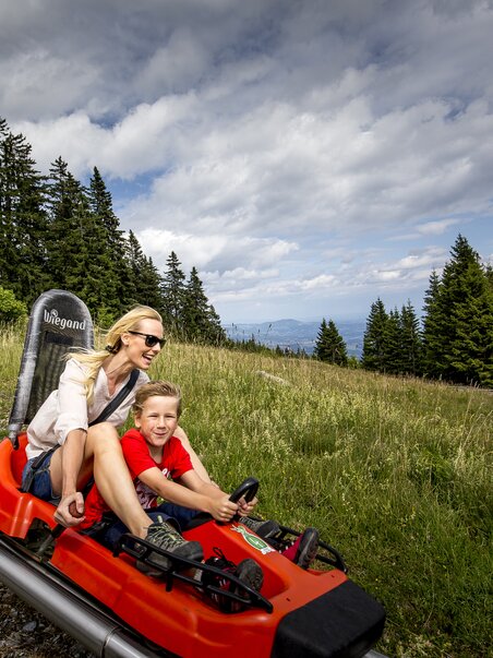 Una madre e suo figlio in slitta estiva tra le montagne. | © Region Graz - Tom Lamm
