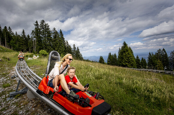 A mother and her son ride a summer toboggan in the mountains. | © Region Graz - Tom Lamm