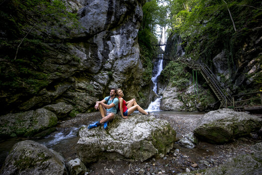 Ein Paar sitzt auf einem Felsen neben einem Wasserfall in der Kesselfallklamm. | © Region Graz - Tom Lamm